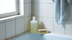 Bagno con piastrelle bianche, spazzola, dispenser e asciugamano azzurro vicino alla finestra.